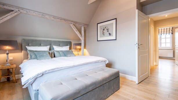 A bedroom with a large bed, a bedside table, a lamp, and a framed artwork on the wall. - House SyltZauber, Germany (Sylt)