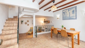 A spacious interior with a wooden staircase, a dining area with a table and chairs, and a view of the outside through a glass door.
