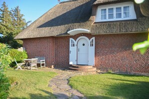 A brick house with a thatched roof, a white front door, and a small porch with steps leading up to it. - Petit Dünenhof, Germany (Kampen (Sylt))