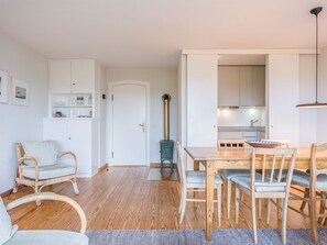 Una sala de estar acogedora con una mesa de comedor de madera, sillas y un sofá. Se observa una cocina al fondo con armarios blancos y una estufa.