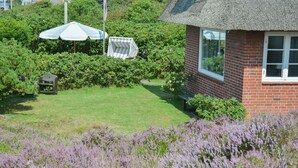 A house with a thatched roof, a brick exterior, and a well-maintained garden with a lawn and lavender bushes. - Kleiner Dünenhof, Germany (Kampen (Sylt))