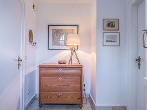 Un couloir avec une commode en bois, une lampe et des œuvres d’art encadrées accrochées au mur.
