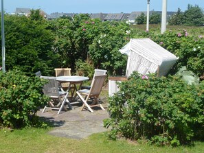 An outdoor seating area with a round table and four chairs, surrounded by lush greenery and flowering bushes. - Petit Dünenhof, Germany (Kampen (Sylt))