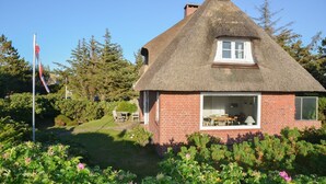 A thatched-roof house with a brick exterior, a visible window, and a flagpole with a flag. - Kleiner Dünenhof, Germany (Kampen (Sylt))