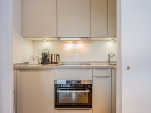 A compact kitchen with white cabinetry, a built-in oven, and a coffee maker on the countertop. - Petit Dünenhof, Germany (Kampen (Sylt))