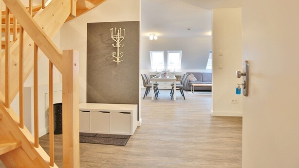 Een modern interieur met een houten trap, een eethoek met een witte tafel en stoelen, en een grijze muur met een decoratieve kandelaar.