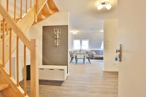 Ein modernes Interieur mit einer Holztreppe, einem Essbereich mit weißem Tisch und Stühlen sowie einer grauen Wand mit einem dekorativen Kerzenleuchter.