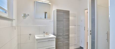 Un baño moderno con lavamanos, espejo y mueble de almacenamiento blanco.