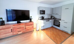 A modern kitchen with a flat-screen TV, wooden cabinetry, a microwave, and a stove. - Strandresidenz Juliusruh apartment 4 - large balcony - family-friendly 3-rooms (Breege)