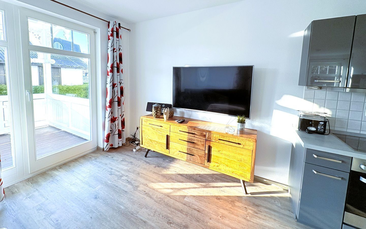 A modern kitchen with a wooden cabinet, a flat-screen TV, and a built-in oven.