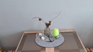 Una mesa con un mantel tejido, un florero con ramas secas, una manzana verde y tres velas pequeñas.