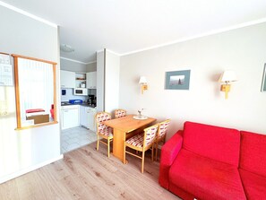 Ein kompakter Wohnbereich mit Essplatz, einem roten Sofa und einer Küche im Hintergrund.