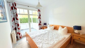 Ein Schlafzimmer mit einem hölzernen Bett, weißer Bettwäsche, einem Nachttisch mit Lampe und Blick auf einen Balkon.
