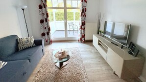 Ein Wohnzimmer mit einer Couch, einem Couchtisch, einem Fernseher und einer Schiebetür zum Balkon.