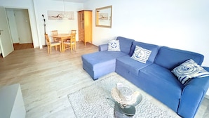 Ein Wohnzimmer mit blauem Sofa, einem Esstisch mit Stühlen und einem Couchtisch mit Dekoration.