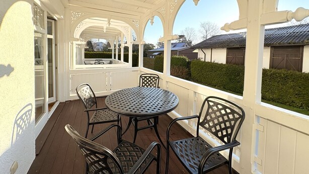 A covered patio with a round table and four chairs, a white exterior wall, and a view of neighboring houses. - Strandresidenz Juliusruh apartment 11- ground floor, balcony, 2 bedrooms - family friendly (Breege)