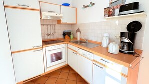 A compact kitchen with a refrigerator, oven, sink, and a coffee maker. - Strandresidenz Juliusruh apartment 11- ground floor, balcony, 2 bedrooms - family friendly (Breege)