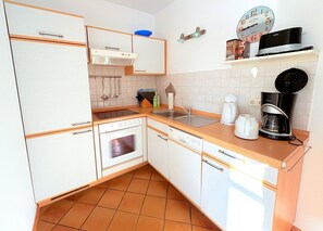 Eine kleine Küche mit Kühlschrank, Backofen, Spüle und Kaffeemaschine.