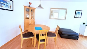 A dining area with a round wooden table, four chairs, a cabinet, and a black ottoman. - Strandresidenz Juliusruh apartment 11- ground floor, balcony, 2 bedrooms - family friendly (Breege)