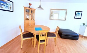 Ein Essbereich mit einem runden Holztisch, vier Stühlen, einem Schrank und einem schwarzen Hocker.