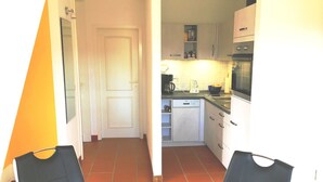 A compact kitchen with white cabinets, a dishwasher, and a microwave. There is a dining table with two chairs. - Fewo Ostseelaune - directly by the forest and the sea - Ostseelaune - Comfortable apartment (Dranske)