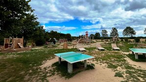 An outdoor playground with various play structures, including slides and climbing frames, set in a grassy area with trees in the background. - Fewo Ostseelaune - directly by the forest and the sea - Ostseelaune - Comfortable apartment (Dranske)