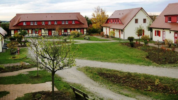 A traditional European-style building with a red and white facade, surrounded by a well-maintained garden and a paved pathway. - Fewo Ostseelaune - directly by the forest and the sea - Ostseelaune - Comfortable apartment (Dranske)