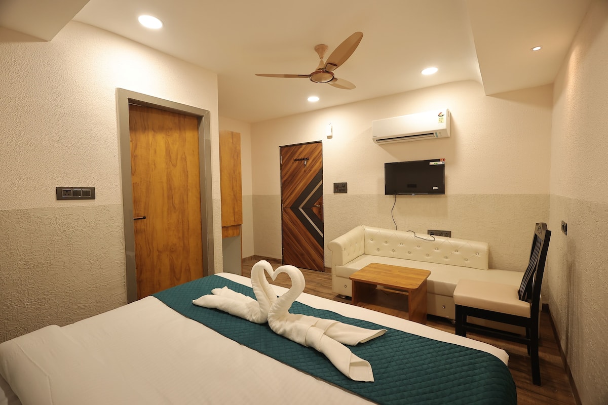 Habitación de hotel con cama, sofá, una mesita, ventilador de techo y aire acondicionado.