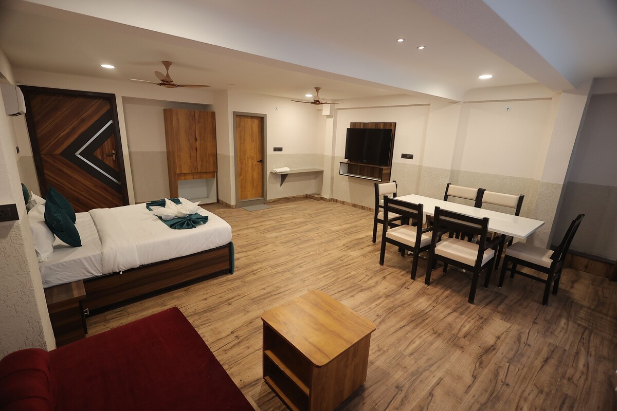 Una habitación moderna y luminosa con una cama, una mesa de comedor con sillas, una pequeña mesa de madera y un televisor montado en la pared.
