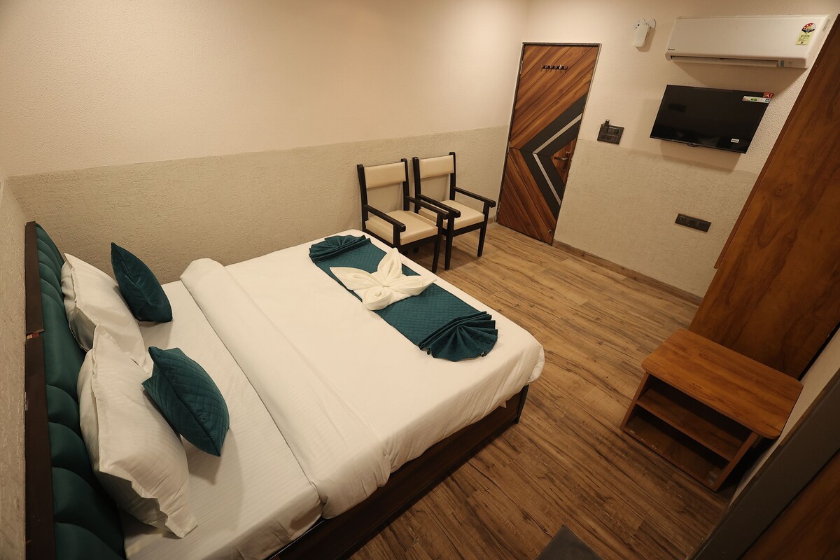 Una habitación de hotel con una cama, dos sillas, un televisor y una puerta de madera.