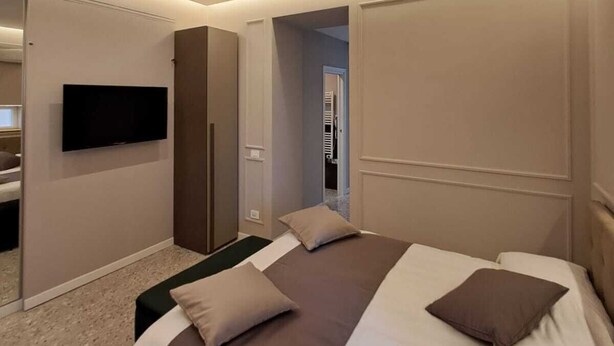 A modern hotel room with a large bed, a flat-screen TV mounted on the wall, and a walk-in closet. - Delightful beachfront apartment equipped with all the comforts (Lido di Ostia)