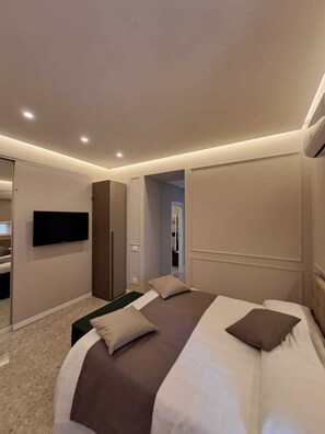A modern hotel room with a large bed, a flat-screen TV mounted on the wall, and a walk-in closet. - Delightful beachfront apartment equipped with all the comforts (Lido di Ostia)