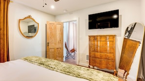A bedroom with a bed, wooden dresser, mirror, ceiling fan, and a TV mounted on the wall. - Historic Pioche Retreat | Near Trails & Cathedral Gorge (Pioche)