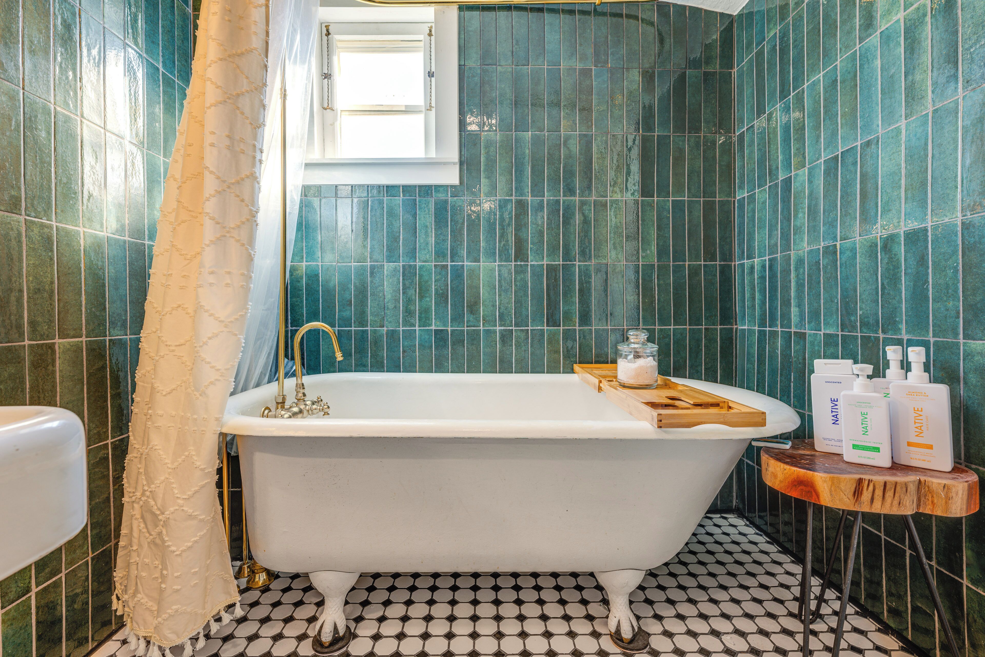 A bathroom with a freestanding bathtub, a wooden side table with toiletries, and a patterned floor.