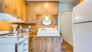 A kitchen with wooden cabinets, a white stove, a sink, and a refrigerator. - Historic Pioche Retreat | Near Trails & Cathedral Gorge (Pioche)