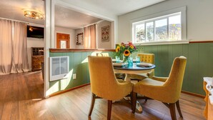 A dining area with a round table, yellow chairs, and a vase with flowers. There is a window with a view of the outdoors. - Historic Pioche Retreat | Near Trails & Cathedral Gorge (Pioche)