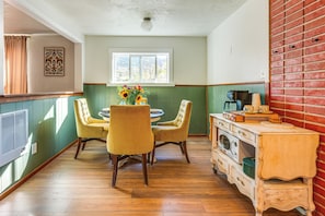 A kitchen with a dining table, chairs, a window, a brick wall, and a wooden cabinet.