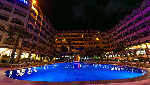 A hotel with a large illuminated pool, multiple balconies, and a central slide. - Golmar Beach& Spa Hotel (Marmaris)