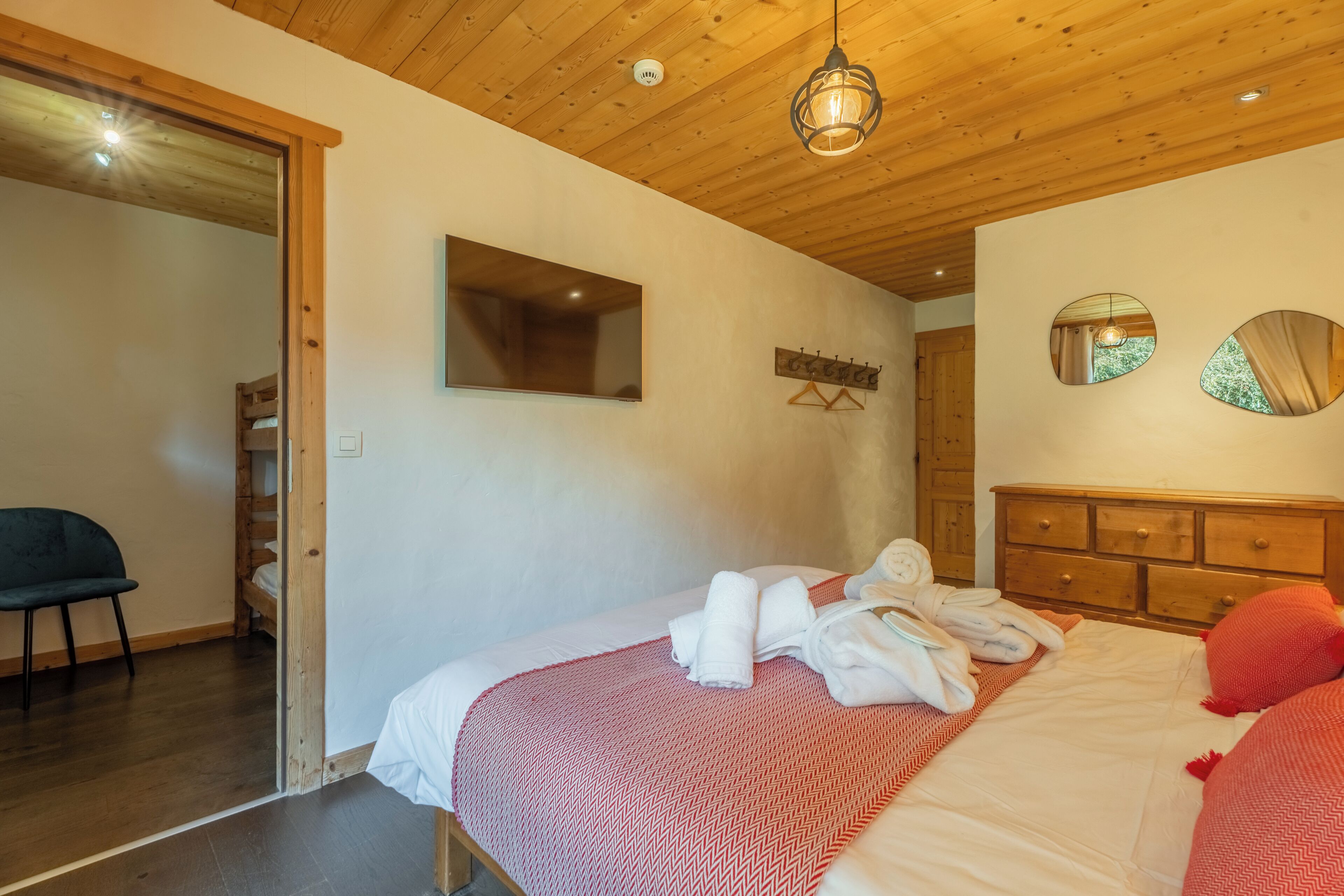 A bedroom with a wooden ceiling, a bed with white bedding, a mirror, and a wooden dresser.