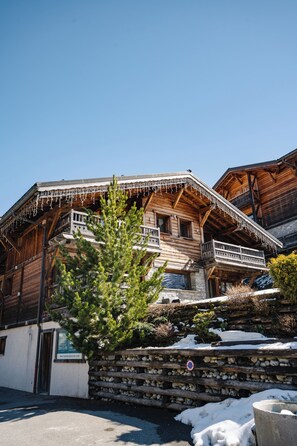 A traditional wooden chalet with balconies, stone walls, and snow on the ground. - Hameau des clos Virolet (Les Gets)