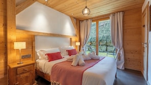 A wooden cabin-style bedroom with a bed, nightstands, and a window with curtains. - Hameau des clos Virolet (Les Gets)