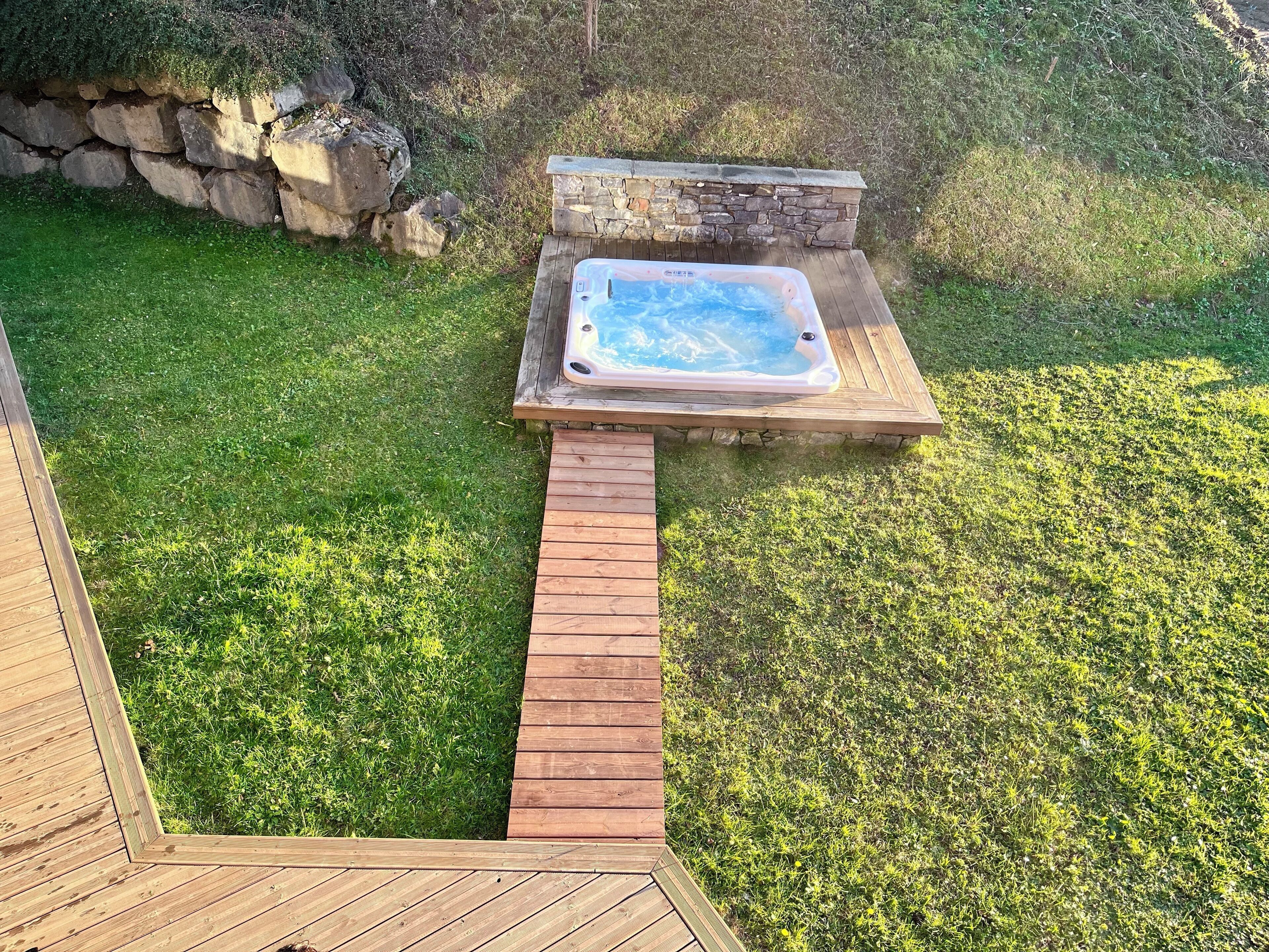 A hot tub on a wooden deck with a stone wall backdrop.