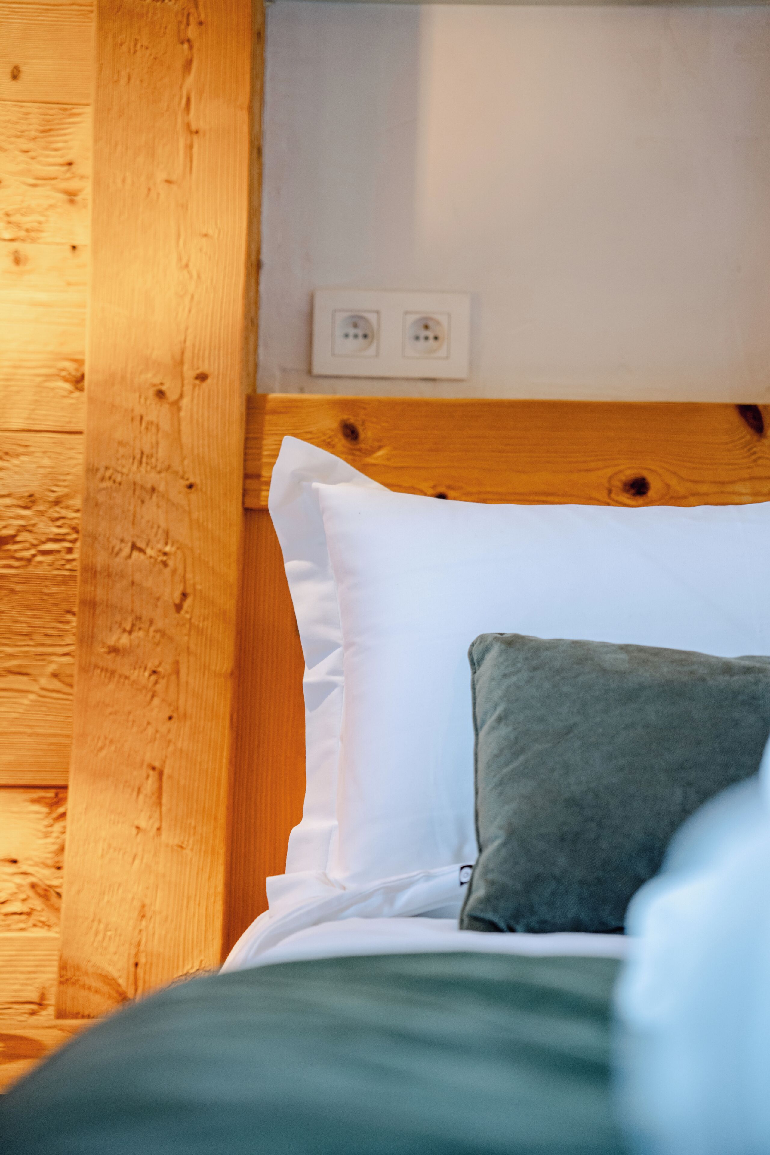 A wooden headboard, white pillows, and a green pillow on a bed.