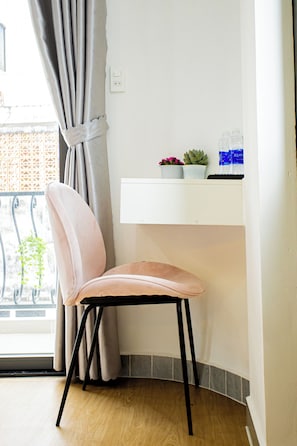 Una habitación de esquina con una silla, un pequeño estante con plantas y una ventana con cortinas.
