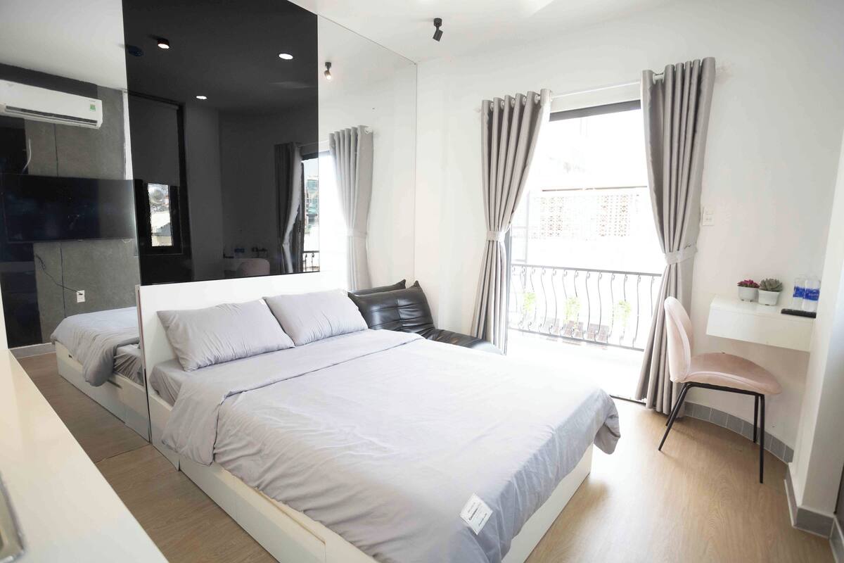A modern bedroom with a large bed, a desk, and a balcony with curtains.