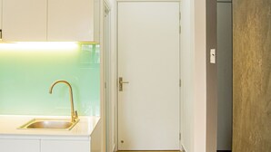 Een keuken met witte kastjes, een gootsteen en een aanrecht. Er is een deur naar een andere kamer.