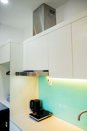Una cocina moderna con gabinetes blancos, una campana extractora de acero inoxidable, una cafetera negra y un salpicadero en color turquesa.