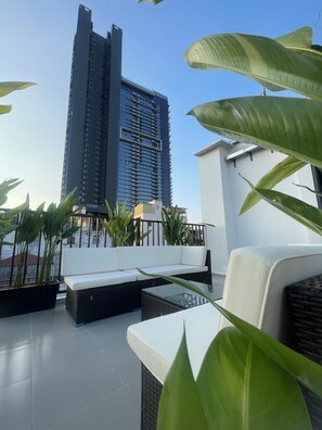 A rooftop terrace with a white sofa, a glass table, and potted plants. A tall building is in the background. - Unite StayCation Nguyen Trai (Ho Chi Minh City)