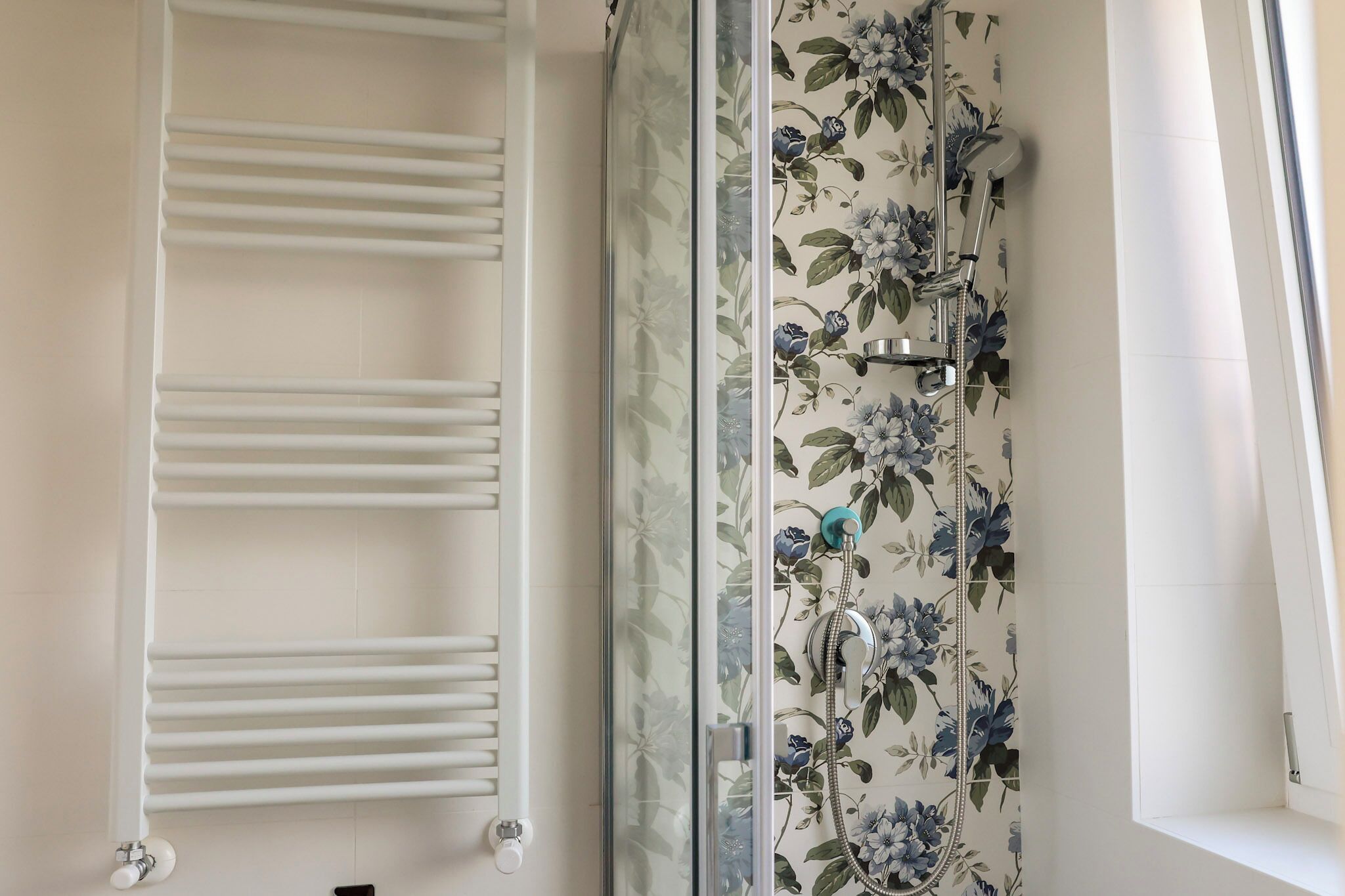 A bathroom with a glass shower enclosure, a white towel rack, and floral-patterned tiles.
