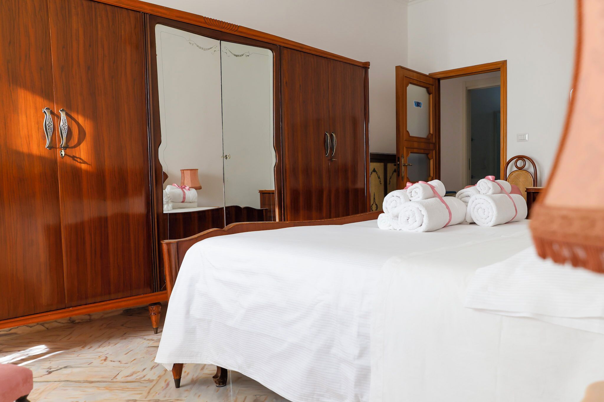 Una camera d'albergo con un ampio armadio in legno, un letto con lenzuola bianche e uno specchio sopra il letto.